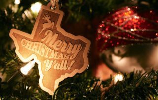 A Texas-shaped ornament that reads "Merry Christmas Y'all!" hangs on a Christmas Tree, marking the Fredericksburg Holidays.